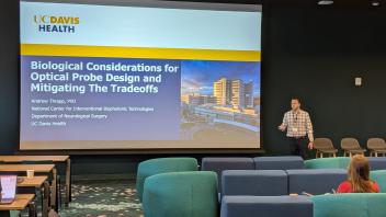 Presenter at podium presenting to audience on biological considerations for optical probe design & mitigating tradeoffs